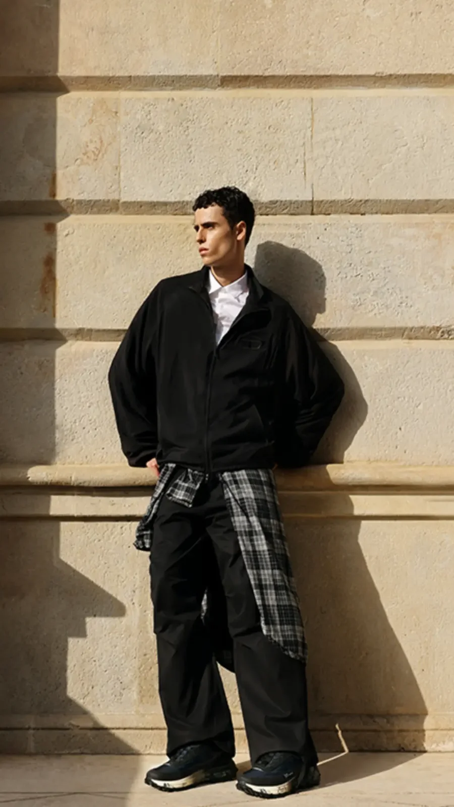 Abrigo negro y pantalón de cuadros en un exterior arquitectónico — estilismo de Manel Guisado