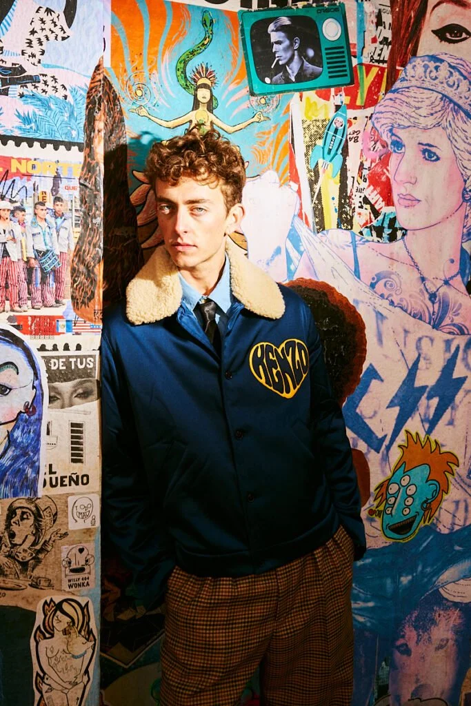 Polo azul y pantalón marrón junto a una pared gráfica — estilismo de Manel Guisado